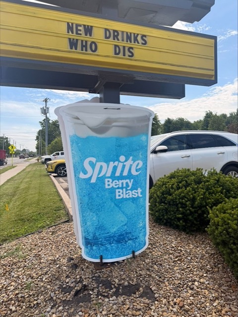 An oversized Sprite Berry Blast cup cutout staked beneath a NEW DRINKS WHO DIS marquee outside the restaurant